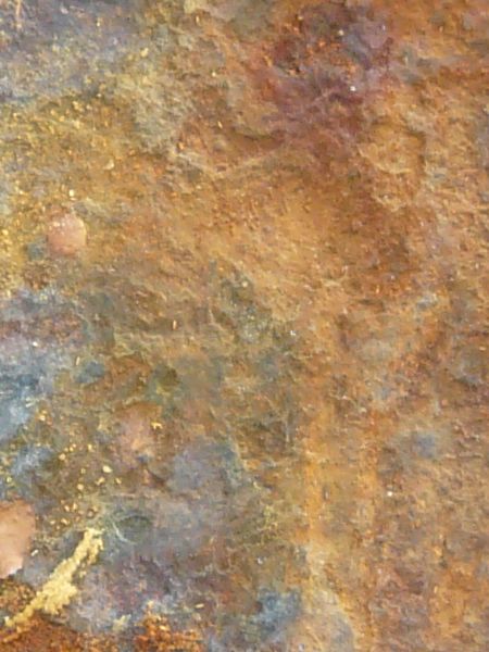 Rusted metal texture, formed into a rough, uneven surface in various hues of blue, yellow and red.